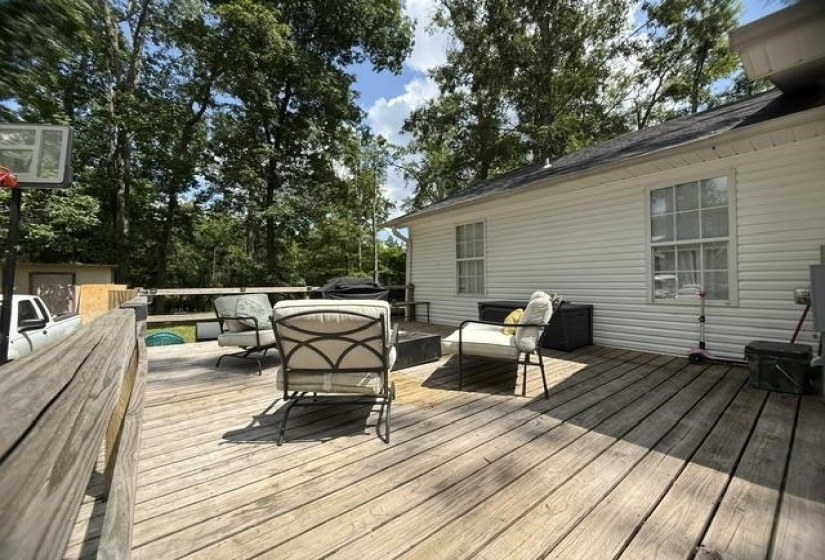 Expansive wooden deck with railing, offering multiple seating areas, set against a backdrop of mature trees
