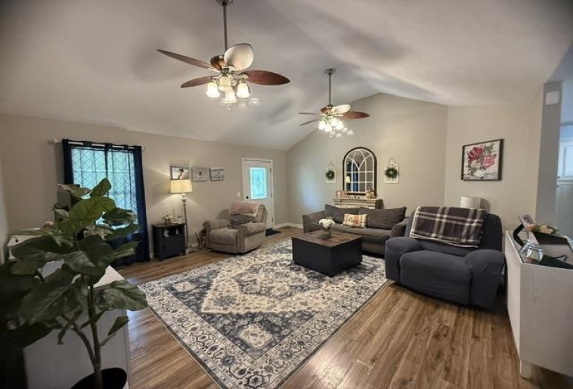 Spacious living area featuring vaulted ceilings, wood-finish flooring, and multiple ceiling fans with integrated lighting
