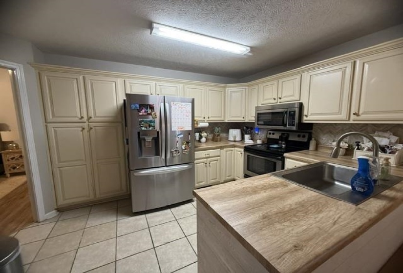 Kitchen featuring extensive cream cabinetry, wood-finish countertops, stainless steel appliances, and diagonal tile flooring