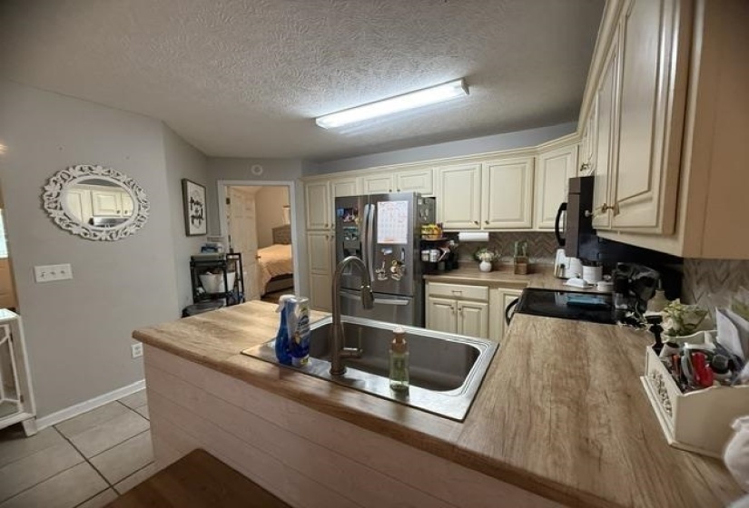 Kitchen featuring wood-finish countertops, stainless steel sink with gooseneck faucet, light cabinetry with gold-tone hardware, and a herringbone-patterned backsplash