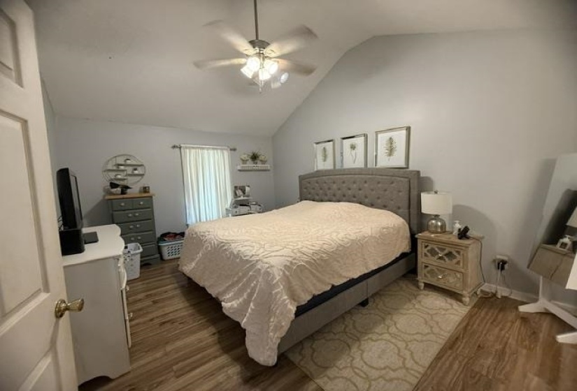 Vaulted ceiling with a ceiling fan light fixture, wood-finish flooring, and a window with white blinds