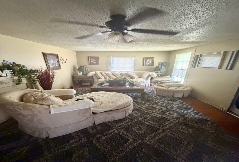 Living area featuring wood-finish flooring, a textured ceiling, and a ceiling fan with integrated lighting