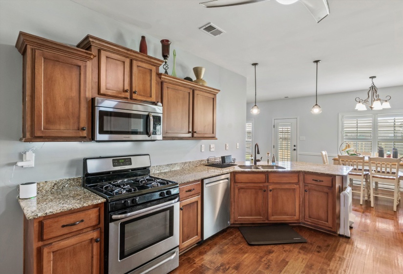 Kitchen featuring wood-finish cabinetry, stainless steel appliances, granite-style countertops, an undermount sink, and wood-finish flooring