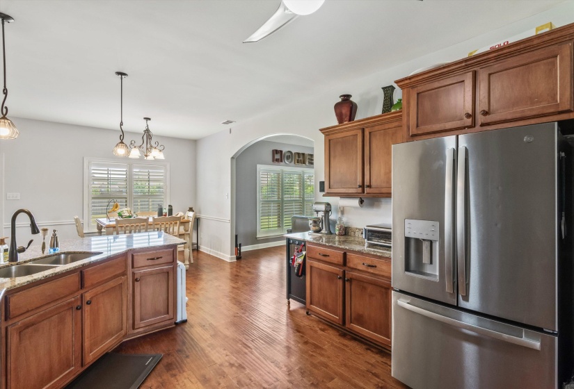 Kitchen featuring wood-finish cabinetry, stone countertops, a stainless steel refrigerator, and a double basin sink with a gooseneck faucet