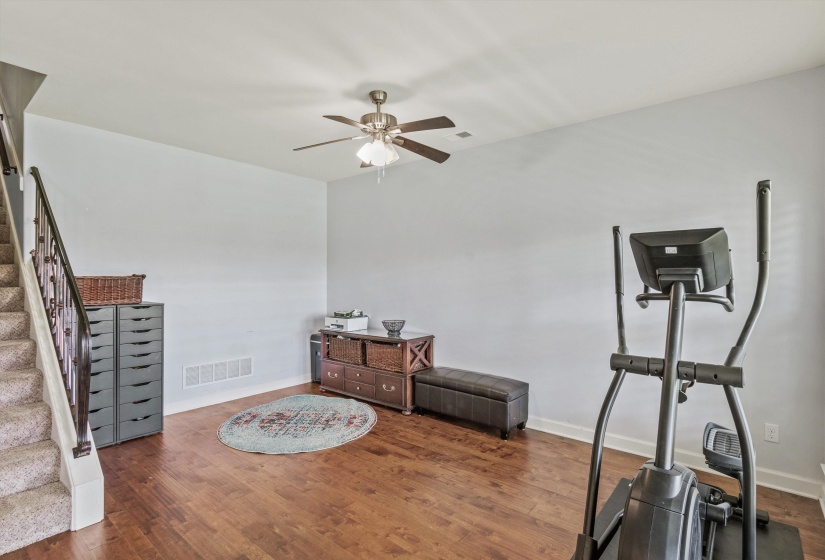 Spacious room featuring wood-finish flooring, a ceiling fan with integrated lighting, and light-toned wall paint