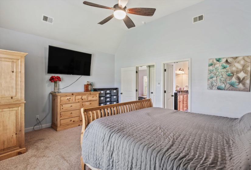 Vaulted ceiling with a ceiling fan, carpeted flooring, and a doorway opening to a bathroom featuring a vanity
