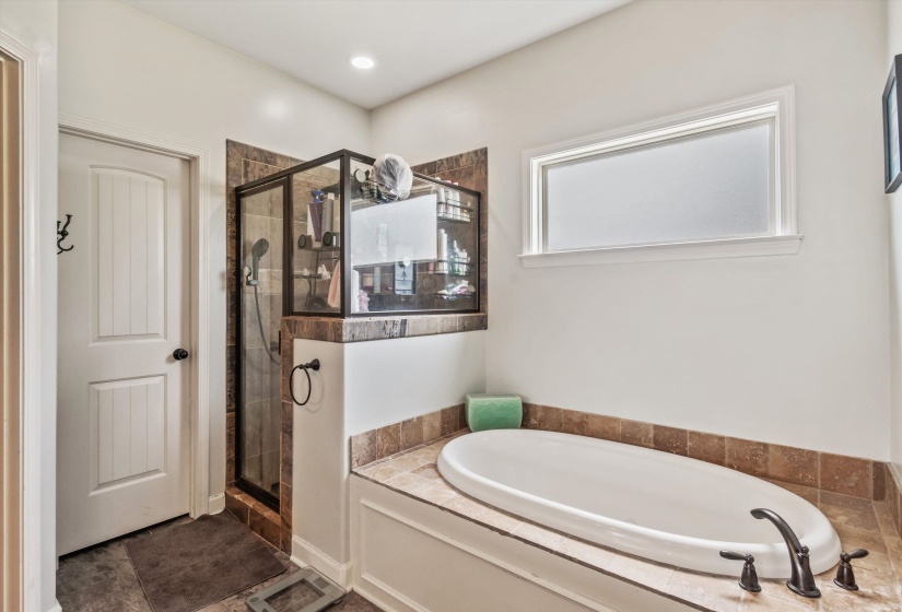 Bathroom featuring a built-in soaking tub with a tiled surround, a separate glass-enclosed shower with full-height tile, and a privacy window