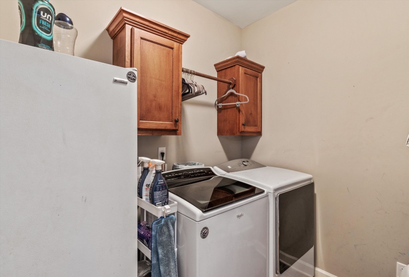 Dedicated laundry area featuring a washer and dryer setup, alongside two wood-finish wall-mounted cabinets, and a horizontal hanging rod