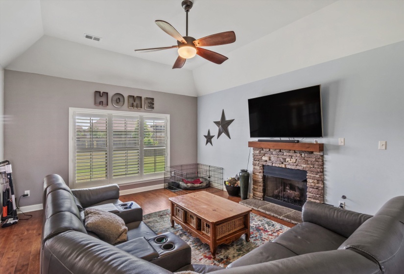 Living area featuring a stone fireplace with a wood-finish mantel, vaulted ceiling with a ceiling fan, and wood-finish flooring