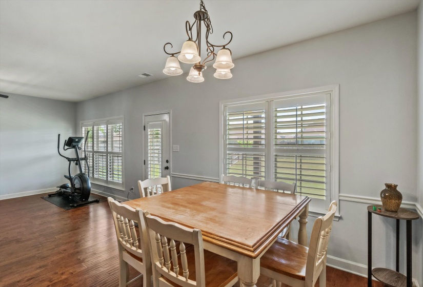 Dining area featuring wood-finish flooring, a decorative overhead light fixture, and white window shutters
