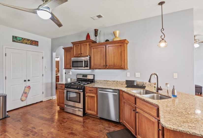 Kitchen featuring wood-finish flooring, stainless steel appliances, granite countertops, wood cabinetry, and a dual-basin sink