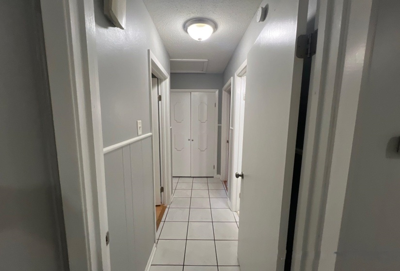 Hallway featuring light gray walls, white wainscoting, and white square floor tiles