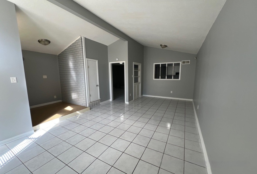Open-concept living area featuring light gray tile flooring, vaulted ceilings, and a neutral color palette