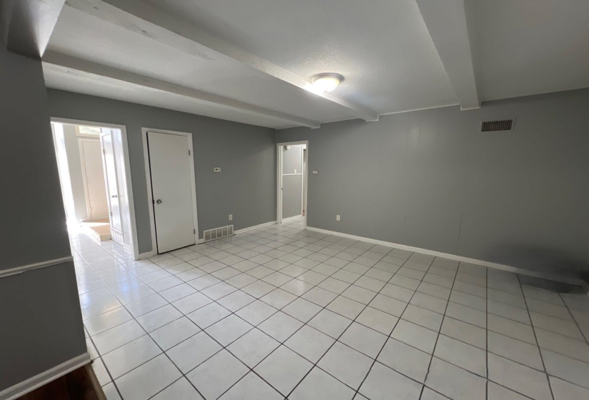 Room featuring light gray walls, exposed ceiling beams, and white square tile flooring