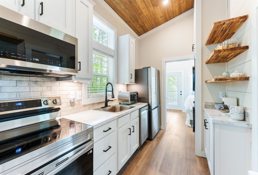 Modern kitchen featuring white cabinetry, stainless steel appliances, a tile backsplash, wood-finish flooring, and a vaulted wood-plank ceiling