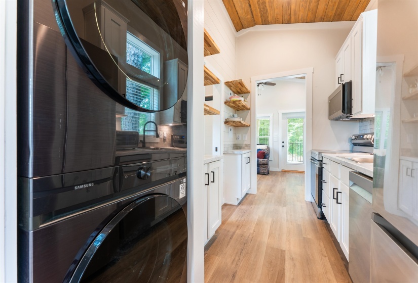 Galley kitchen featuring white cabinetry, light-tone wood-finish flooring, stainless steel appliances, and a vaulted ceiling with wood paneling