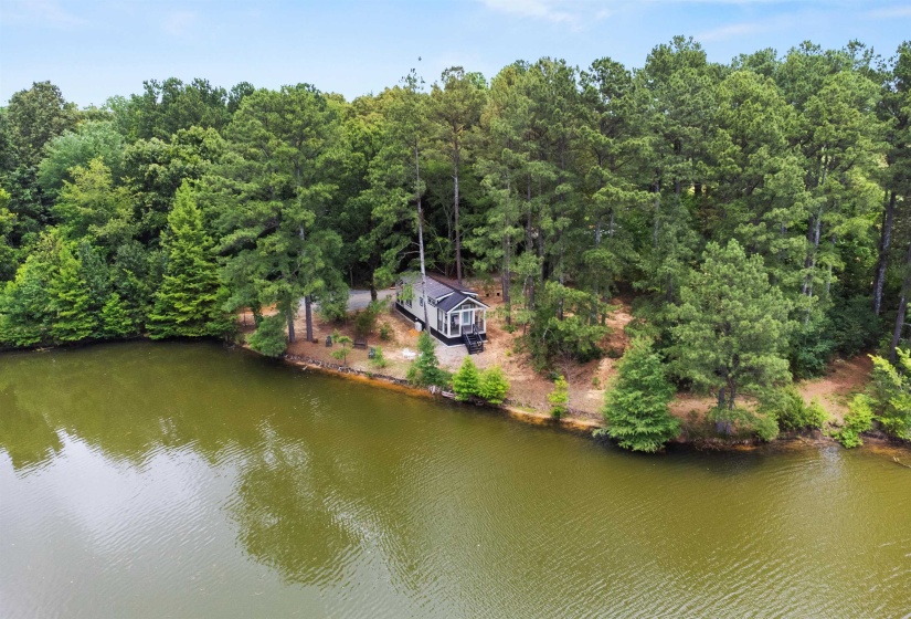 Waterfront property featuring a contemporary structure with a dark-toned exterior, surrounded by mature trees