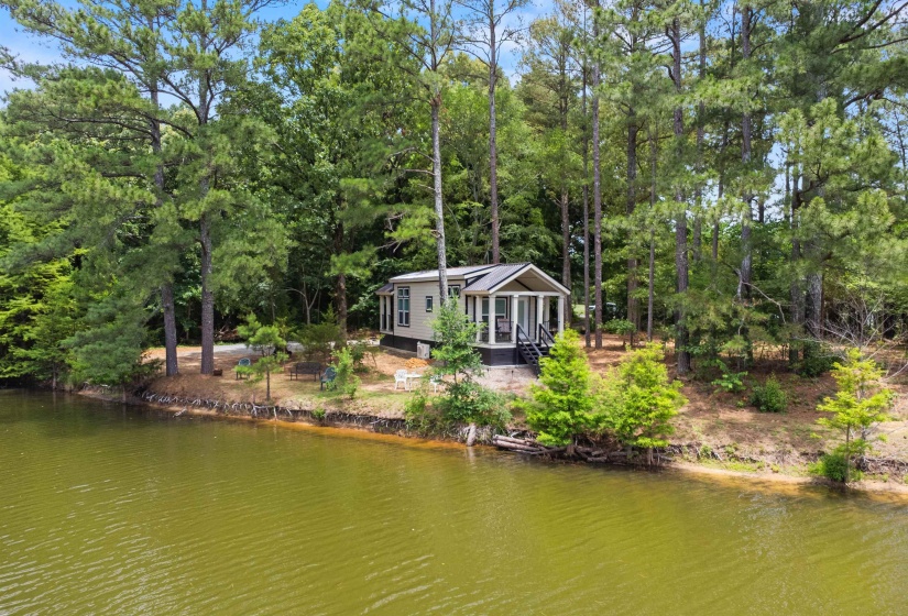 Waterfront property featuring a sunroom with expansive windows, elevated porch with dark railings, and a surrounding natural landscape of mature trees