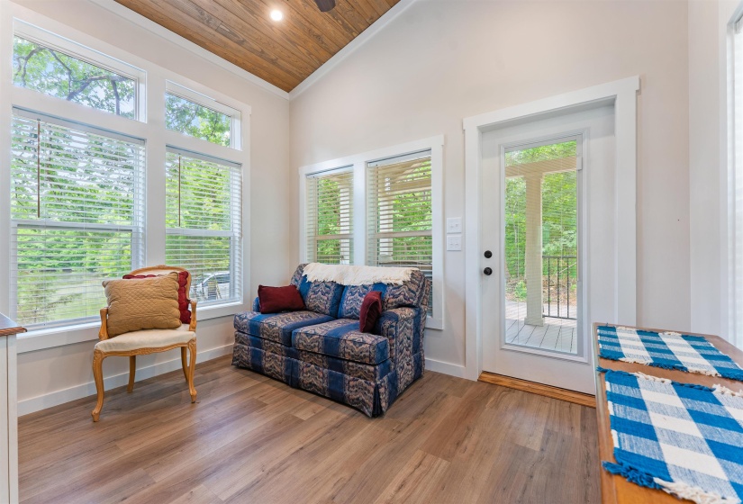 Vaulted wood-finish ceiling with a ceiling fan, abundant natural light through multiple windows, wood-finish flooring, and a glass-paneled exterior door