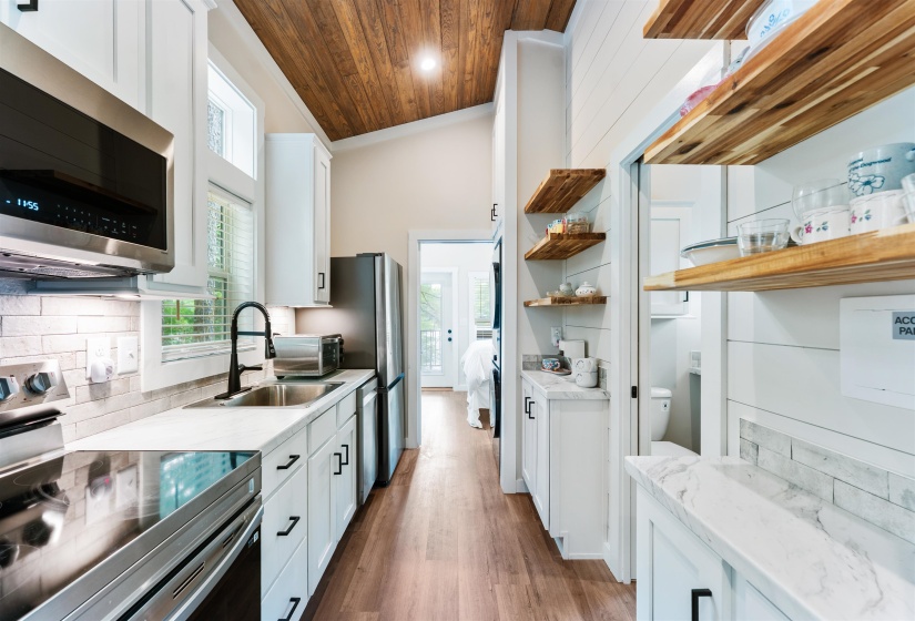 Kitchen featuring a vaulted wood-finish ceiling, stainless steel appliances, white cabinetry with black hardware, and wood-finish flooring
