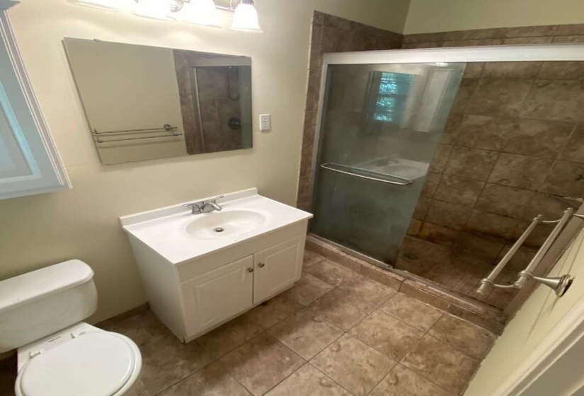 Bathroom featuring a glass-enclosed shower with tile surround, a white vanity with an integrated sink, a wall-mounted mirror, and a three-light fixture