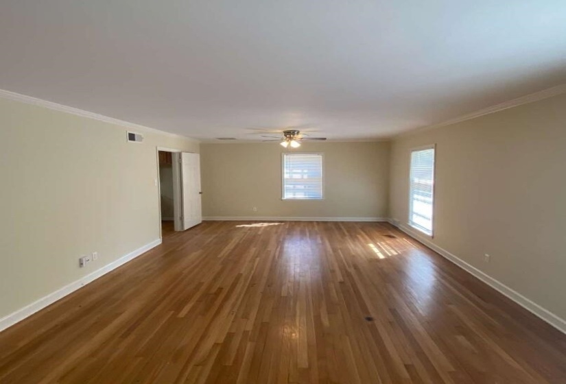 Spacious room featuring wood-finish flooring, two windows with blinds, a ceiling fan with integrated lighting, and white baseboards