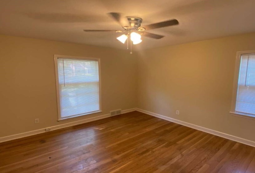 Room featuring hardwood flooring, two windows with blinds, a ceiling fan with integrated lighting, and neutral wall tones