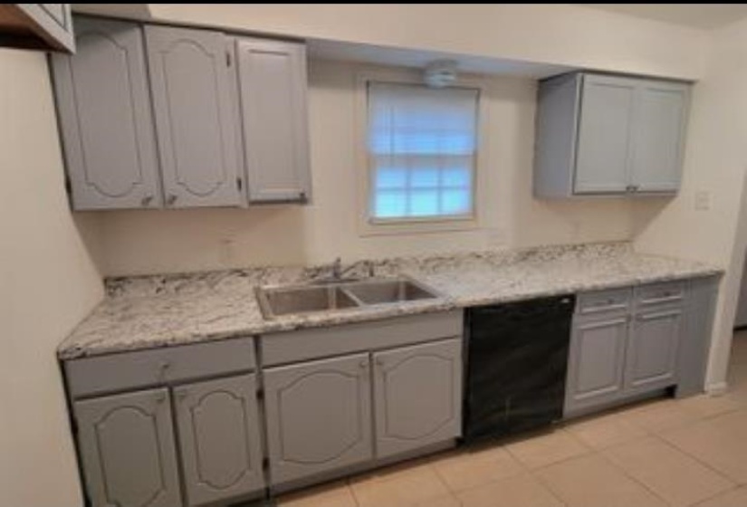 Updated kitchen featuring gray cabinetry, light-toned countertops, a double basin stainless steel sink, and a black built-in dishwasher