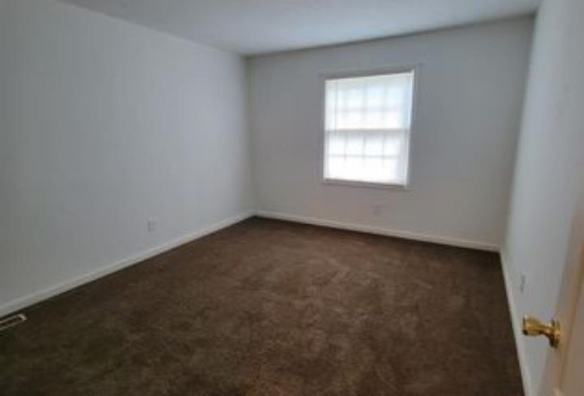 Bedroom featuring neutral wall paint, brown carpeting, baseboard trim, a single window with blinds, and a brass-finish door handle