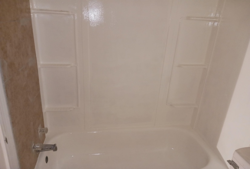 Bathtub featuring a white acrylic surround, integrated shelving, and a chrome faucet with clear knob handles