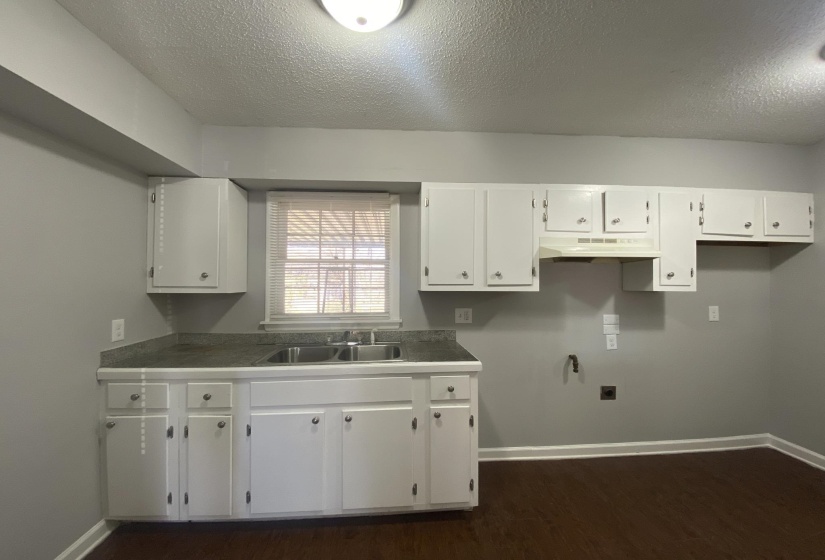 Kitchen with white cabinetry, a double basin stainless steel sink, a range hood, and wood-finish flooring