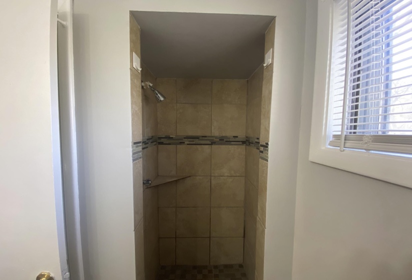 Tiled shower enclosure featuring a mosaic accent band, integrated corner shelf, and a shower head