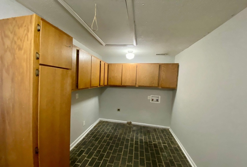 Utility room featuring extensive wood-finish cabinetry, brick flooring, a ceiling-mounted light fixture, and appliance hookups