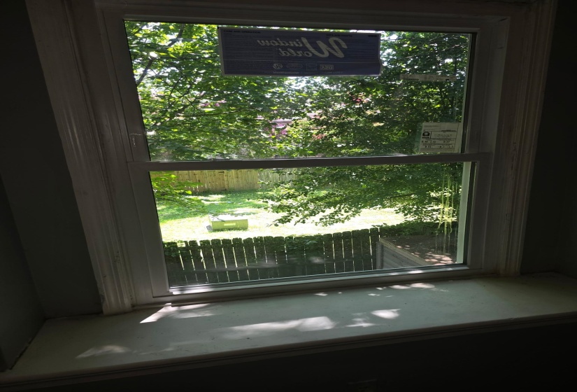 Double-hung window with a classic white frame and substantial sill, offering a bright outlook to the private backyard with a wood fence and mature trees