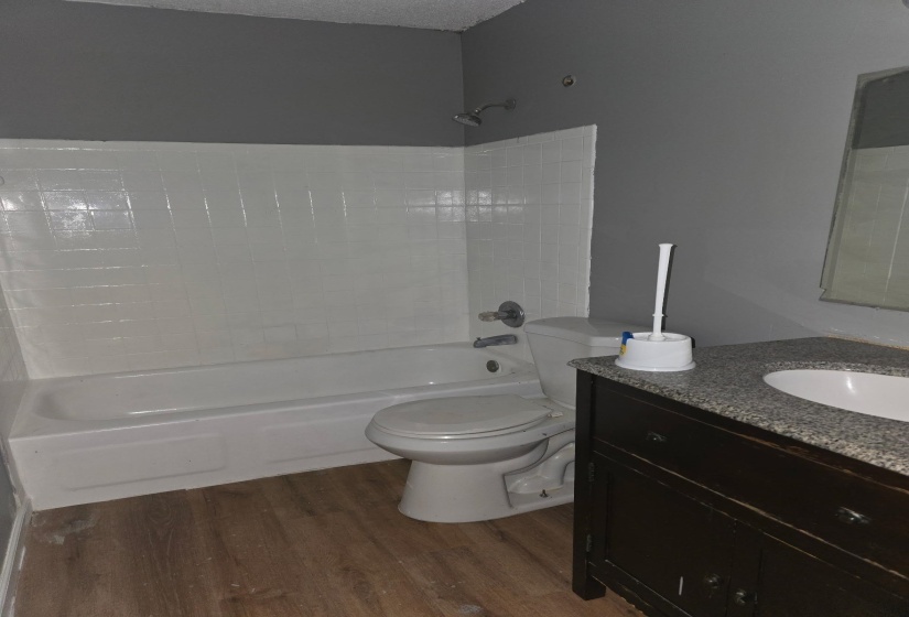 Bathroom featuring a white bathtub and shower surround, a white toilet, and a dark wood-finish vanity with a light speckled countertop and a white undermount sink