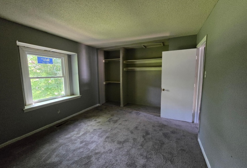 Room featuring a double-hung window, built-in shelving, carpet flooring, a white interior door, and textured walls