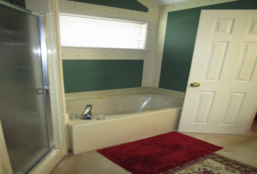 Corner jetted soaking tub featuring a chrome faucet and a frosted glass shower enclosure