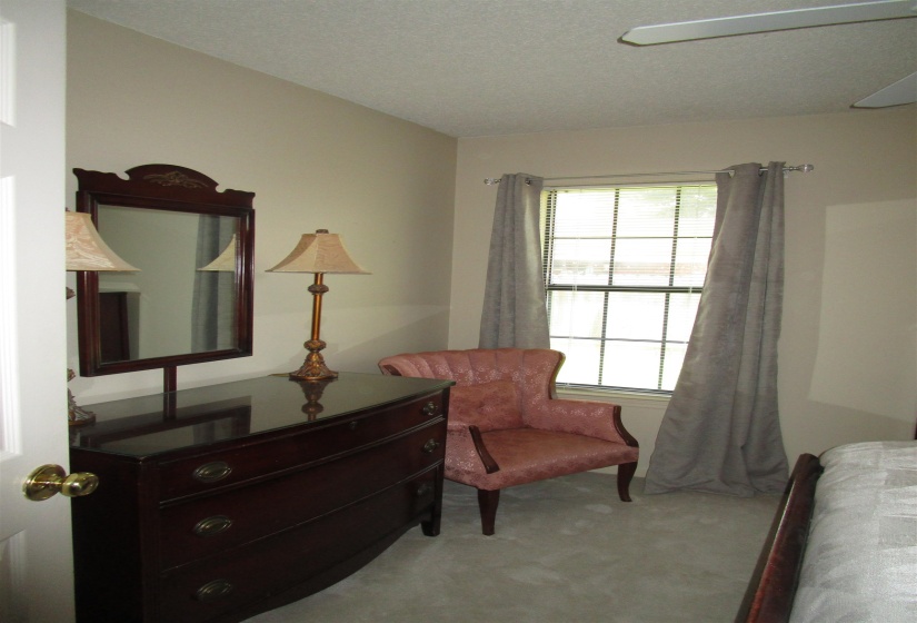 Wall-to-wall carpeting in a neutral tone, featuring a window with horizontal blinds and drapery rods