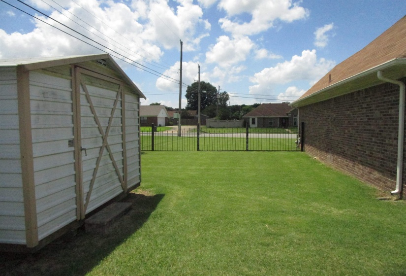 Expansive green lawn featuring a metal storage shed, dark brick exterior, and a black wrought iron fence