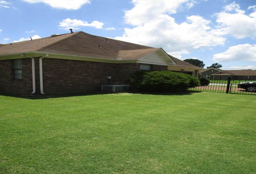 Brick exterior featuring a brown shingle roof, white gutters, and a prominent green lawn