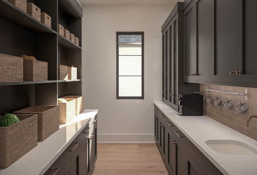 Spacious pantry featuring extensive dark cabinetry with brass hardware, light wood-finish flooring, and a single window