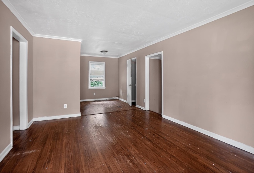 Spacious room featuring wood-finish flooring, neutral-toned walls, white crown molding, and multiple doorways