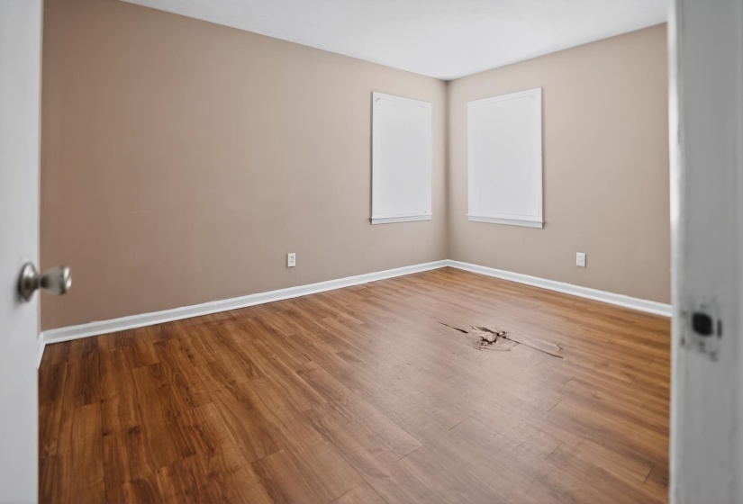 Room featuring two windows with white blinds, light brown walls, and wood-finish flooring