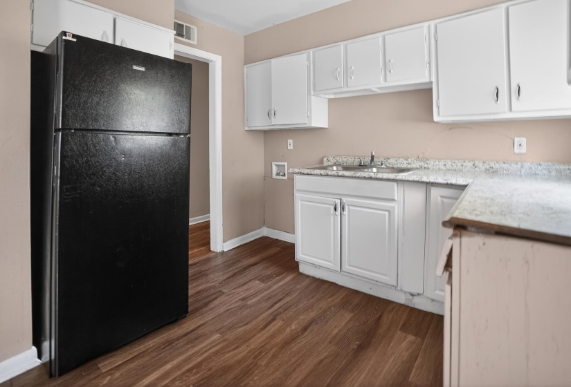 Kitchen area featuring wood-finish flooring, white cabinetry, speckled countertops, and a double basin sink