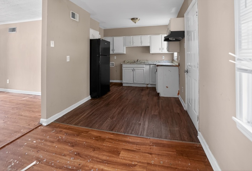 Kitchen with wood-finish flooring, white cabinetry, a black refrigerator, and a dark range hood
