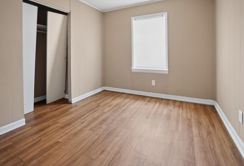 Room featuring wood-finish flooring, neutral wall paneling, white trim, and a window with a white frame