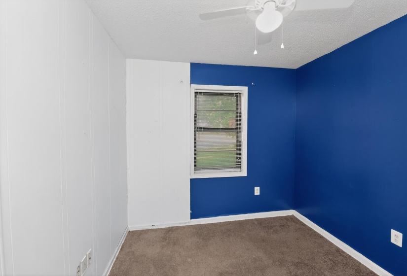 Room featuring white vertical wall paneling, a single window with horizontal blinds, blue painted walls, brown carpeting, and a ceiling fan with integrated lighting