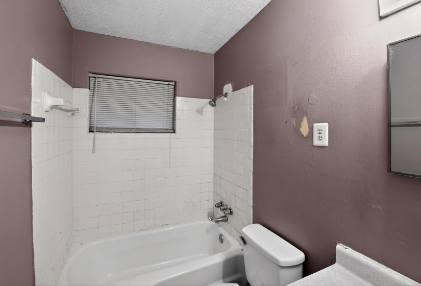 White tiled bathtub and shower combination with a window featuring horizontal blinds