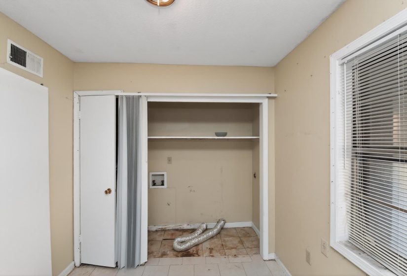 Dedicated utility space featuring an open shelving unit, wall-mounted electrical outlets, and a floor vent