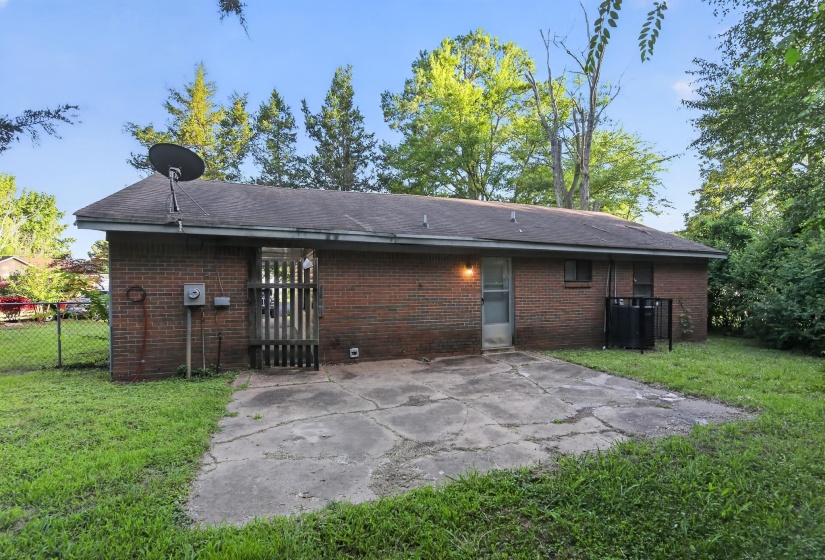 Brick exterior featuring a concrete patio, fenced yard, and mature trees
